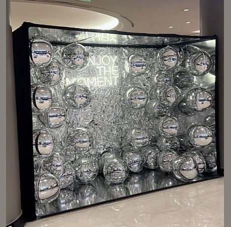 Błyszcząca fotobudka z srebrnymi kulami i neonowym napisem 'Enjoy the moment' w nowoczesnym wnętrzu.