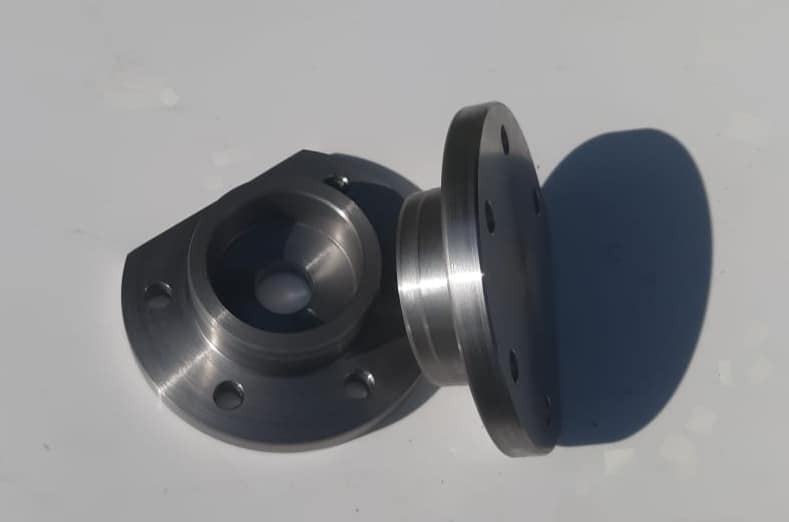 Dwa metalowe elementy kołnierzowe z otworami, wykonane z precyzją, leżące na jasnym tle, widoczne ślady obróbki.