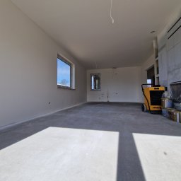 Prace Wykończeniowe - Wnętrze po szpachlowaniu i gładziowaniu ścian, widoczny osuszacz powietrza Master i okna z widokiem na błękitne niebo.