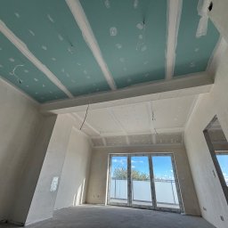 Prace Wykończeniowe - Wnętrze w trakcie prac: sufit z płyt gipsowo-kartonowych, wstępnie wyszpachlowany, widoczne przewody elektryczne. Ściany przygotowane do dalszych prac wykończeniowych.