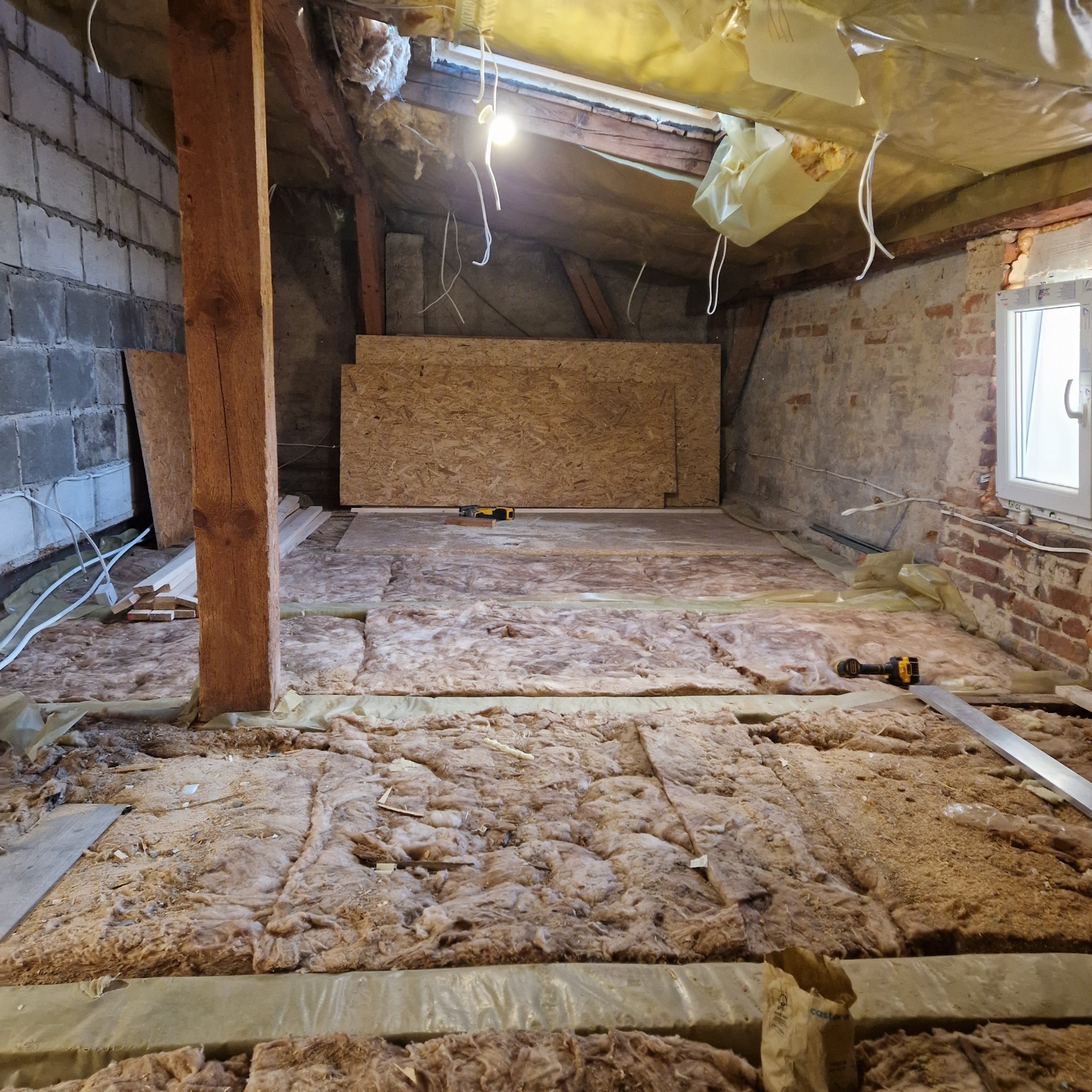 Ocieplenie poddasza wełną mineralną, widoczne płyty OSB, narzędzia i elementy konstrukcyjne dachu.