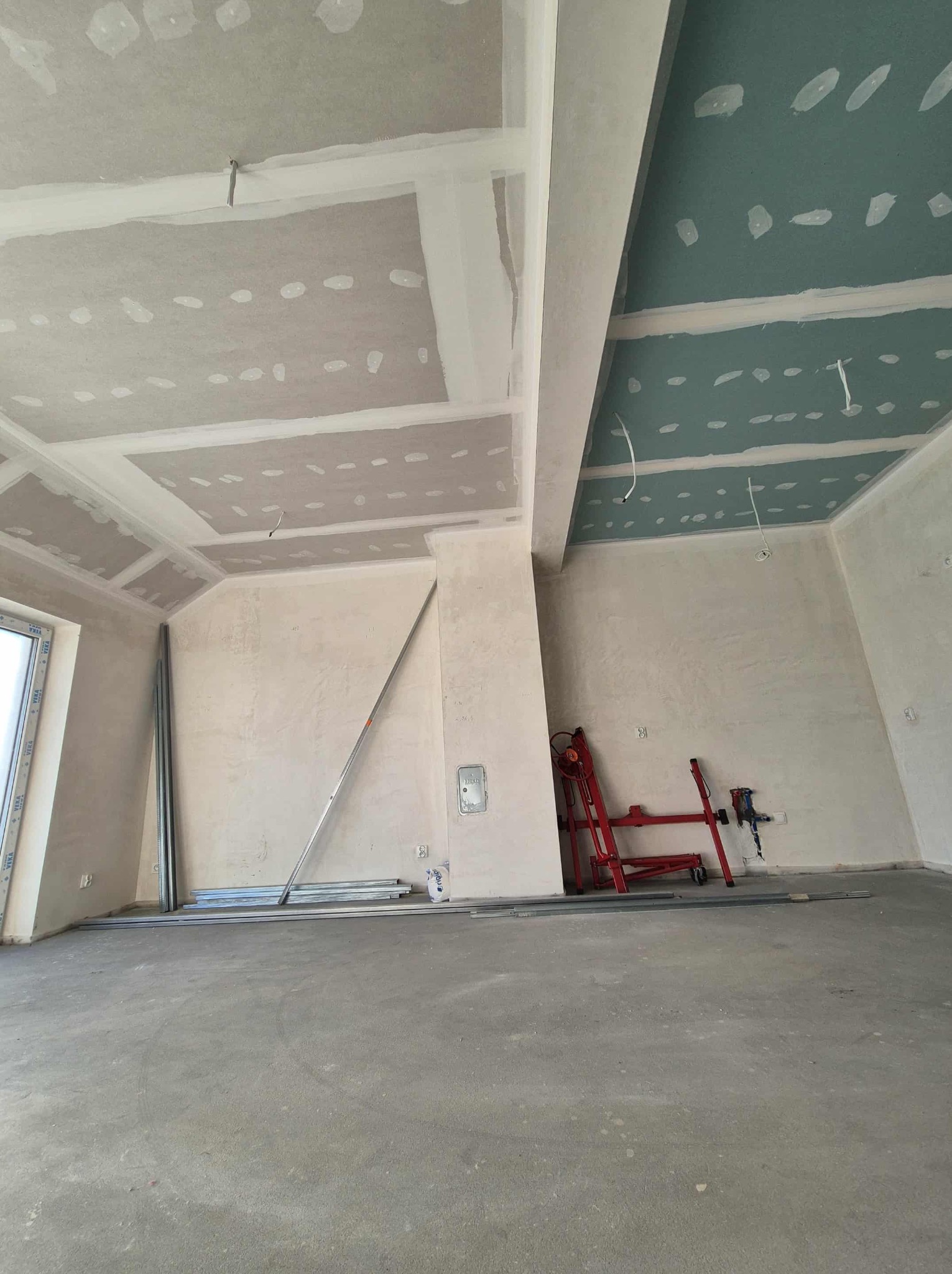 Wnętrze w trakcie prac wykończeniowych: sufit z płyt gipsowych, częściowo pomalowany na zielono, widoczne profile i narzędzia, przygotowane do dalszych prac.