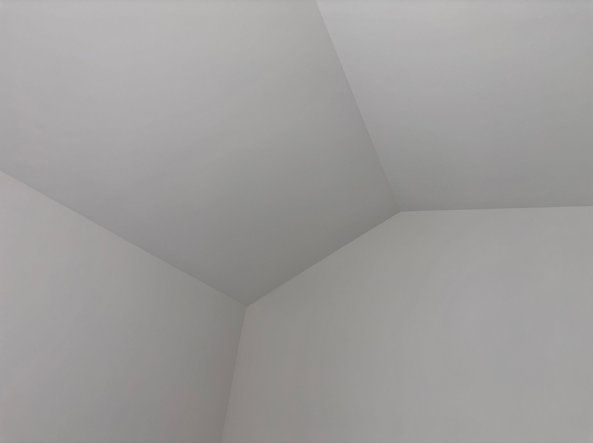 Świeżo pomalowany, jasnoszary narożnik sufitu i ścian. Gładka powierzchnia, minimalistyczne ujęcie z dołu, podkreślające geometrię wnętrza.