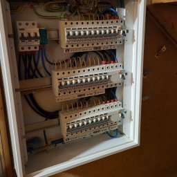 USŁUGI BUDOWLANE POMIARY ELEKTRYCZNE ANDRZEJ ZIMNY - Otwarta rozdzielnica elektryczna z trzema rzędami wyłączników nadprądowych ETI, precyzyjnie ułożonym okablowaniem i peszlami, zamontowana na drewnianej ścianie.