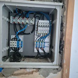 USŁUGI BUDOWLANE POMIARY ELEKTRYCZNE ANDRZEJ ZIMNY - Wbudowana rozdzielnica elektryczna z uporządkowanym okablowaniem i wyłącznikami, osadzona w ścianie z widocznymi cegłami i tynkiem w trakcie prac.