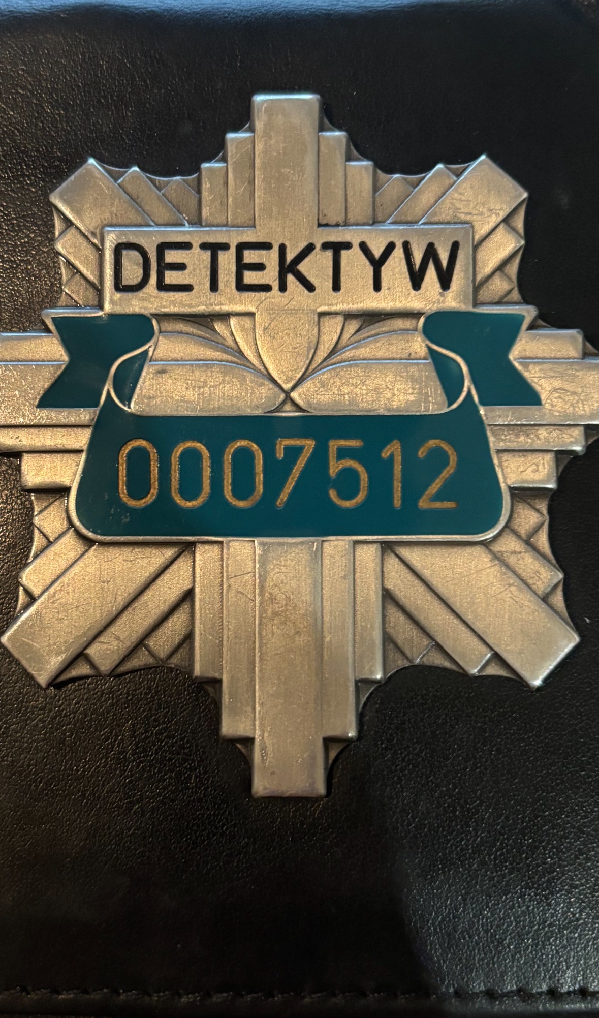 Metalowa odznaka z napisem 'Detektyw' i numerem 0007512 na czarnym, skórzanym tle. Symbol licencji detektywistycznej, gwarantującej profesjonalizm i bezpieczeństwo.