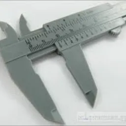 Szary suwmiarka plastikowa, widok z góry pod kątem, skala w milimetrach i calach, na białym tle.