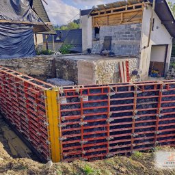 Konstrukt - Szczegółowe ujęcie szalunku fundamentowego w Ciche k. Czarnego Dunajca, z widoczną konstrukcją z czerwonych elementów i czarnych paneli, przygotowaną do zalewania betonem. W tle widać częściowo...