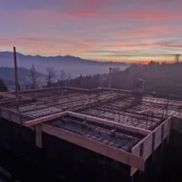 Siatka zbrojeniowa ułożona w szalunku fundamentu na tle malowniczego, wschodzącego słońca nad górami.