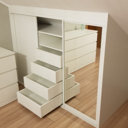 WOODLUCK - Biała szafa wnękowa z lustrzanymi drzwiami przesuwnymi i otwartymi szufladami w kształcie schodków, widoczna na tle poddasza z drewnianą podłogą i komodą.