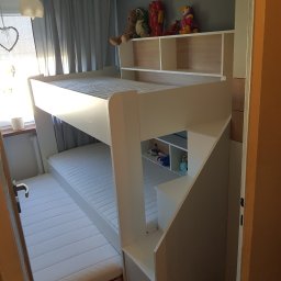 WOODLUCK - Białe łóżko piętrowe z wbudowanymi półkami i schodami, zabawki na półkach, widok z poziomu podłogi.