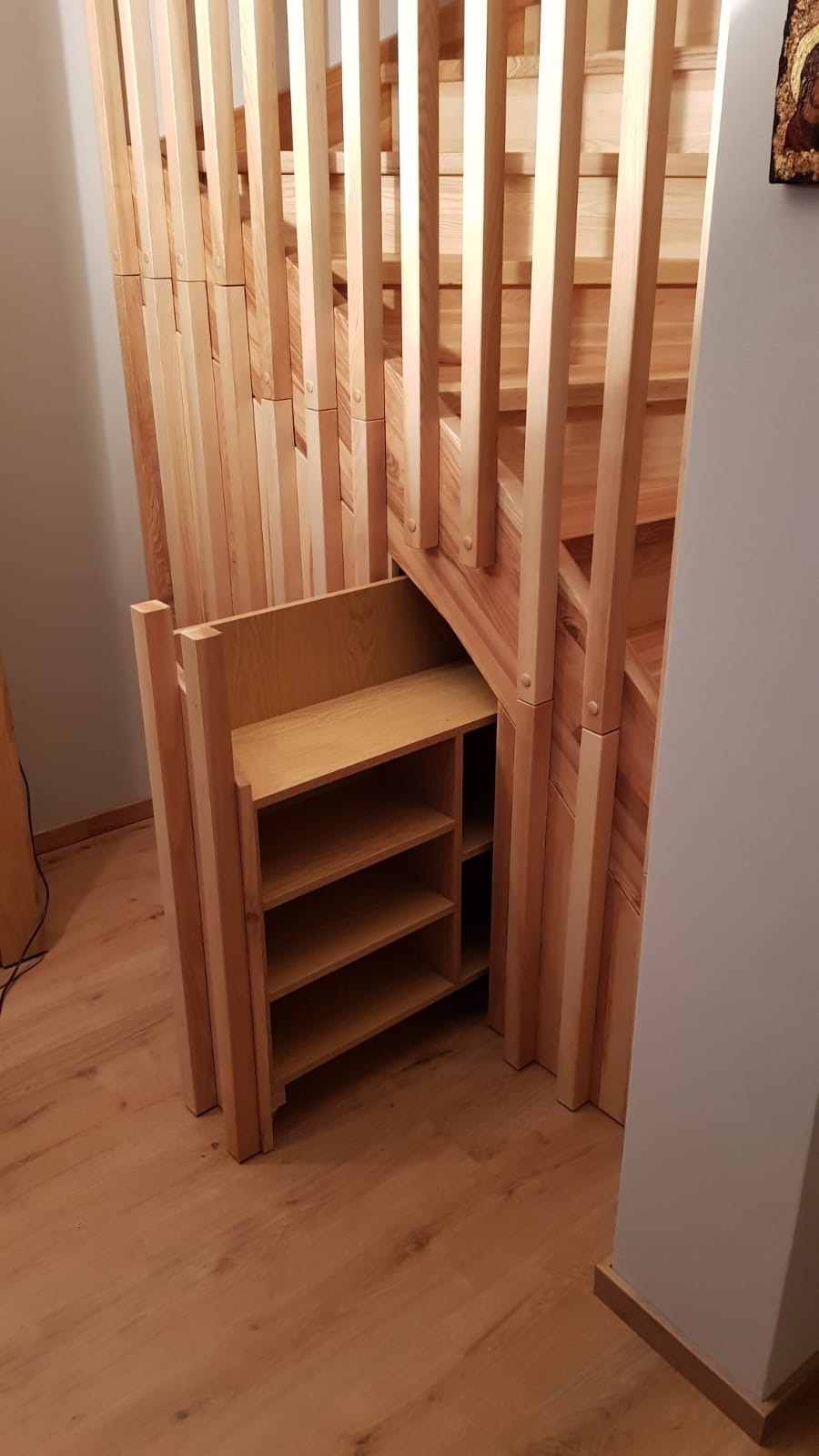Drewniane schody ze schowkiem z półkami pod spodem, widok z boku na jasną podłogę.