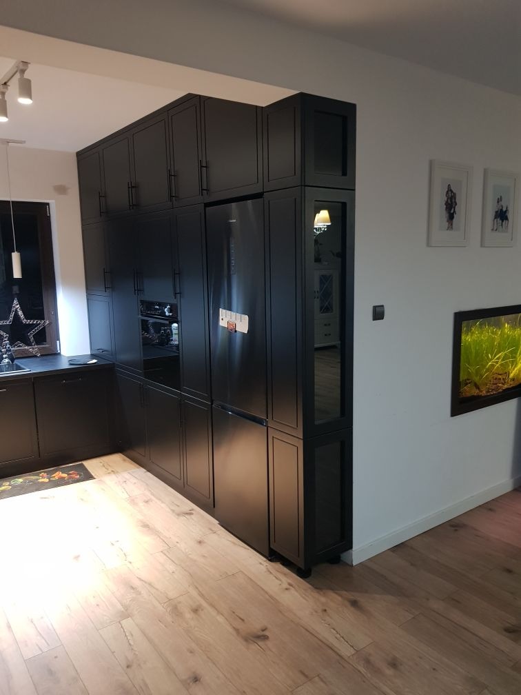 Czarne meble kuchenne na wymiar z lodówką w zabudowie i szklanymi witrynami, oświetlenie punktowe, drewniana podłoga.