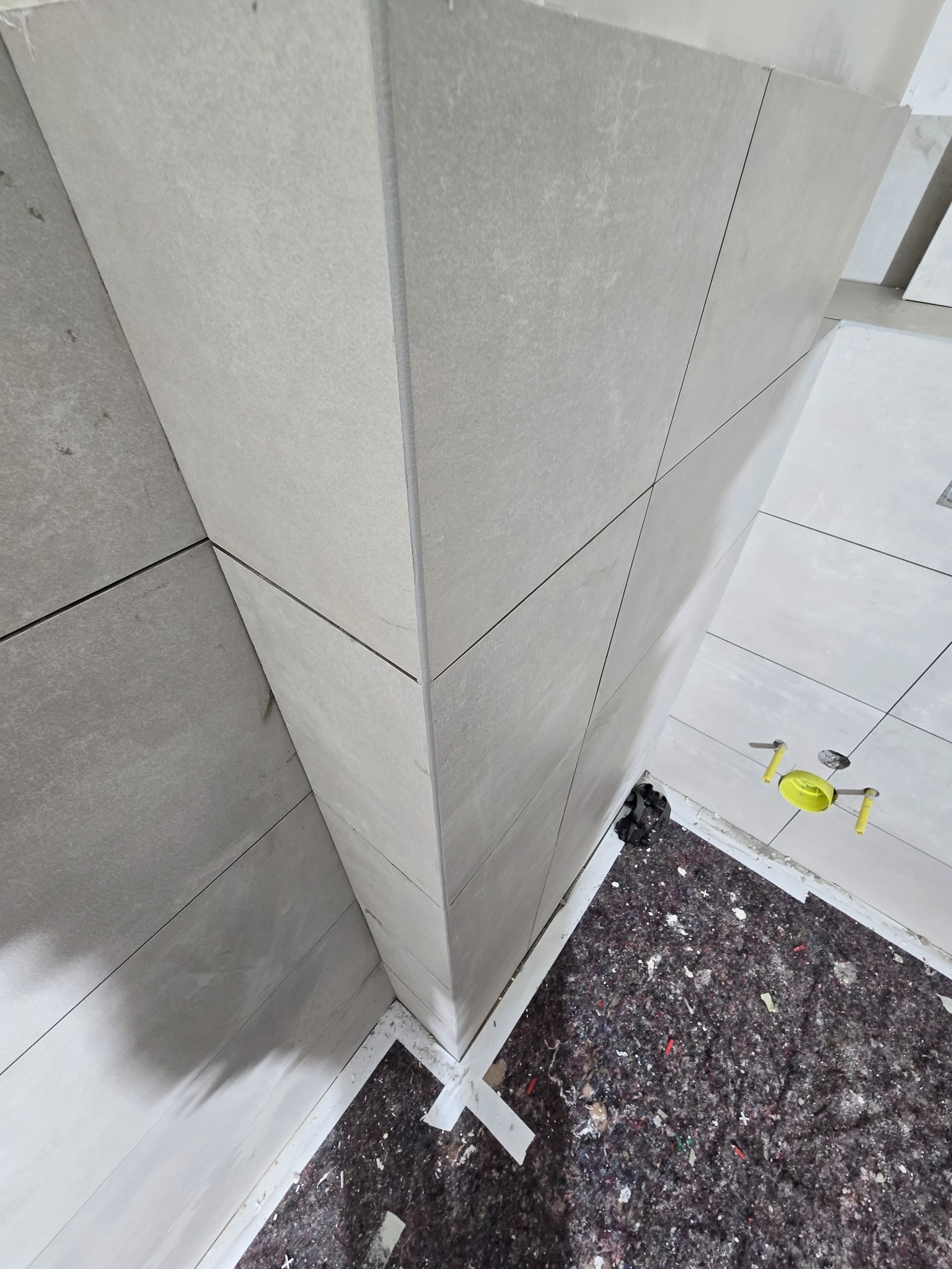 Świeżo ułożone, duże, szare płytki na ścianie i podłodze w łazience, widok z góry na zakryte podłoże i poziomice.