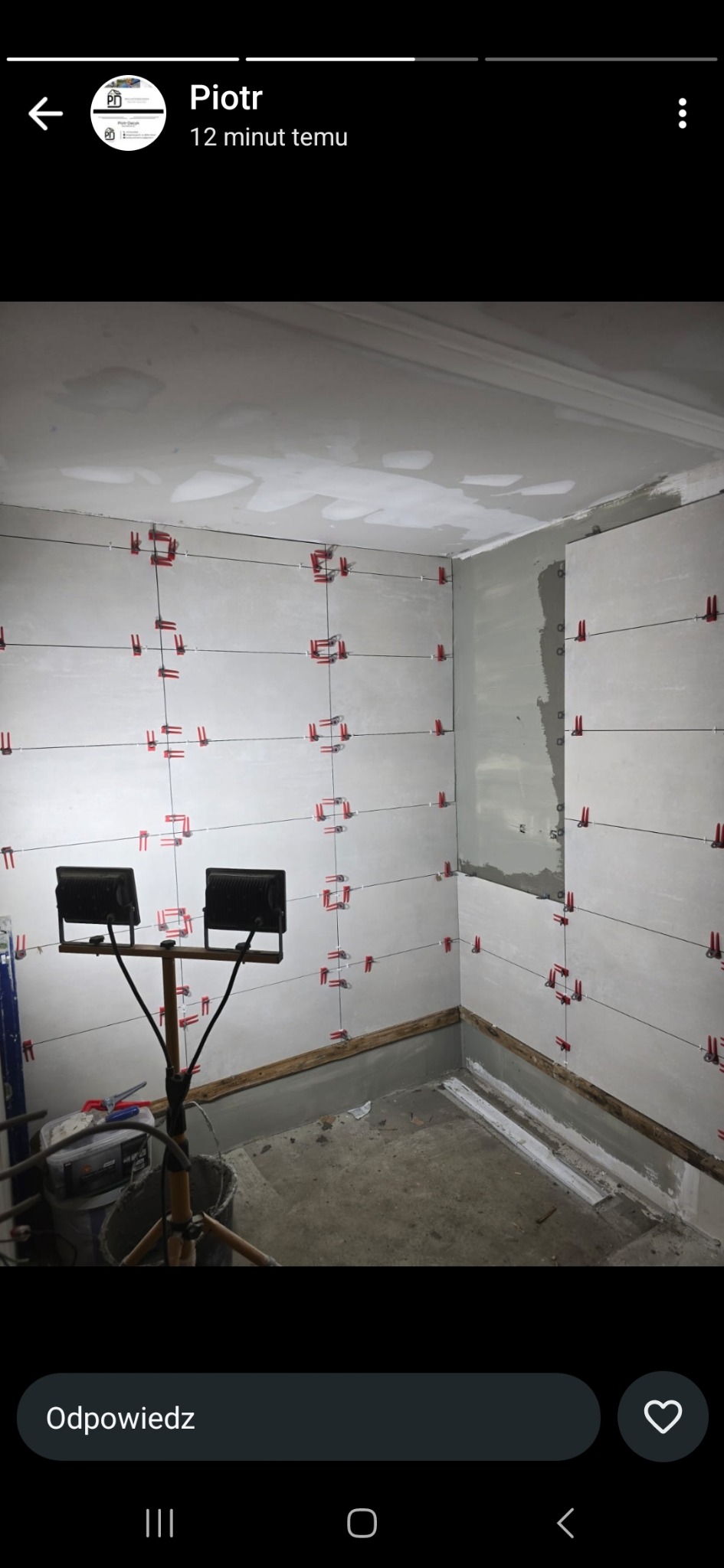 Ściany łazienki w trakcie układania płytek, widoczne krzyżyki dystansowe, oświetlenie robocze i przygotowane podłoże.