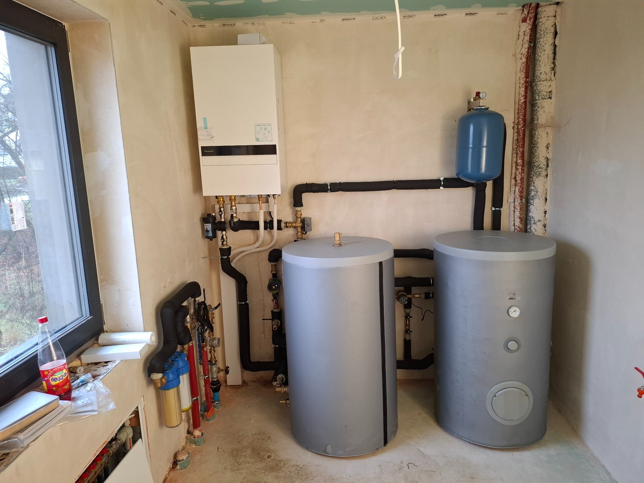 Instalacja pieca gazowego z dwoma zasobnikami ciepłej wody w surowym wnętrzu w Plichtowie, widoczne rury i elementy hydrauliczne.