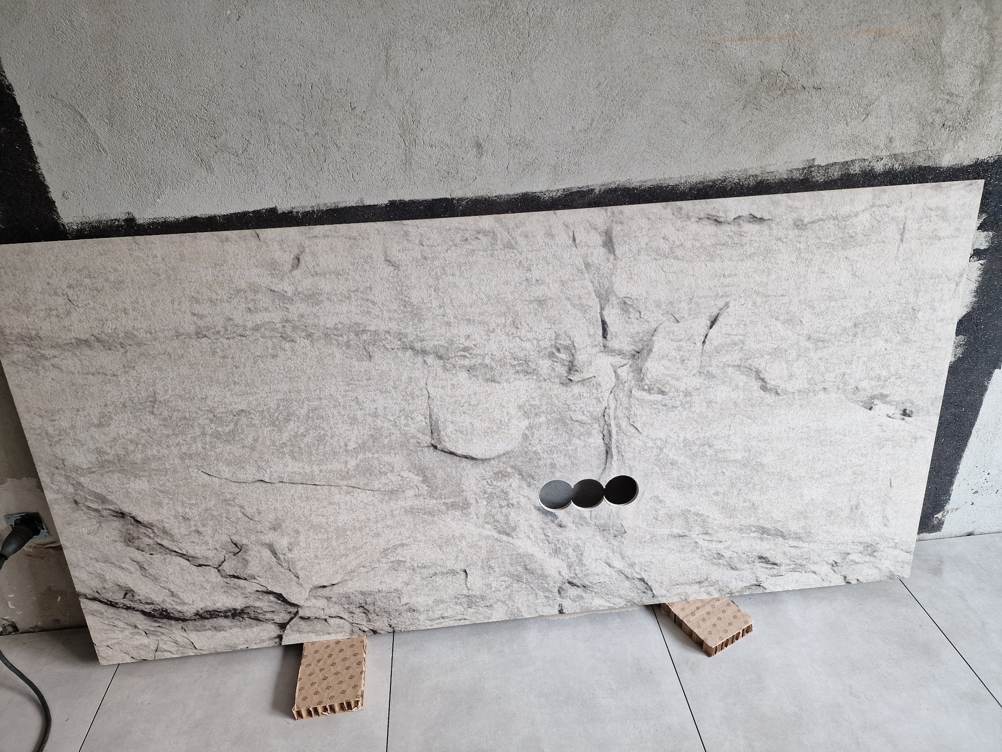 Blat łazienkowy z imitacją kamienia z trzema otworami na baterię, przygotowany do montażu w Ostrzeszowie, podparty na tekturowych elementach.