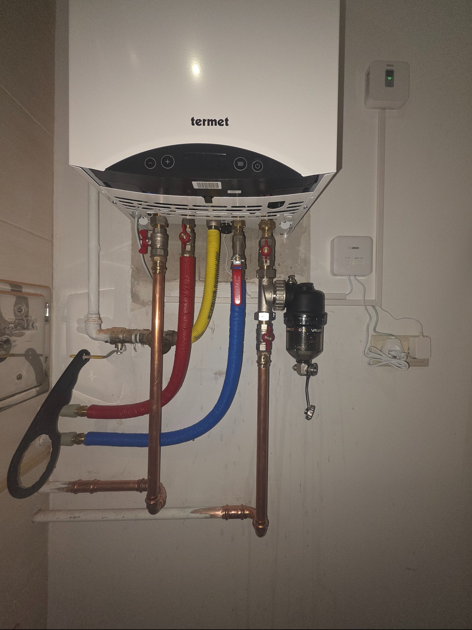 Biały piec gazowy Termet z podłączeniami (miedziane rury, zawory) na ścianie w Sosnowcu. Widoczne elementy instalacji i sterownik.