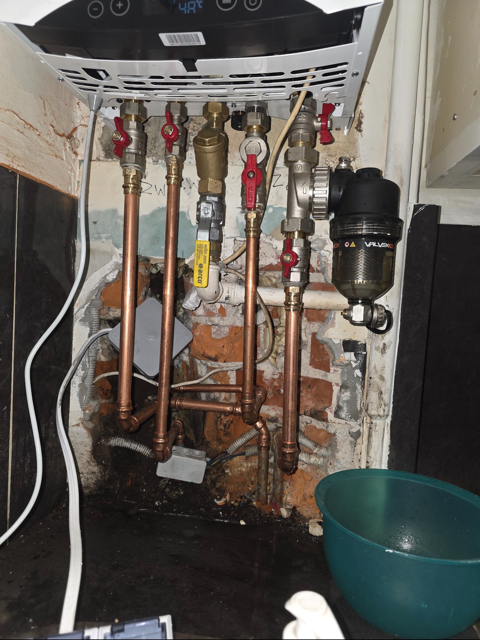 Nowy piec gazowy z miedzianą instalacją, zaworami i filtrem Valvex Pro. Widoczne przyłącza i fragment ściany z cegły.