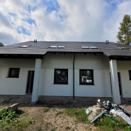 Firma Remontowo-Budowlana Daniel Olek - Świeżo otynkowany dom jednorodzinny z ciemną dachówką i oknami, widoczne ślady po pracach wykończeniowych na trawniku.