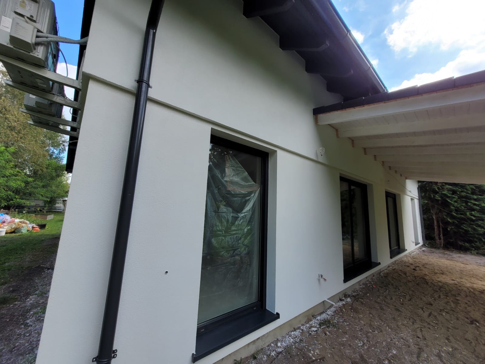 Świeżo otynkowana elewacja domu jednorodzinnego z czarną rynną i oknami zabezpieczonymi folią malarską.