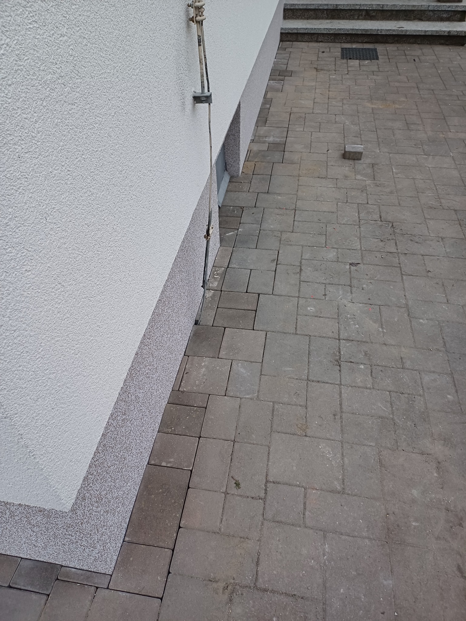 Fragment elewacji budynku z widocznym ociepleniem cokołu i ułożoną kostką brukową na podjeździe, z pojedynczym niedopasowanym elementem kostki.