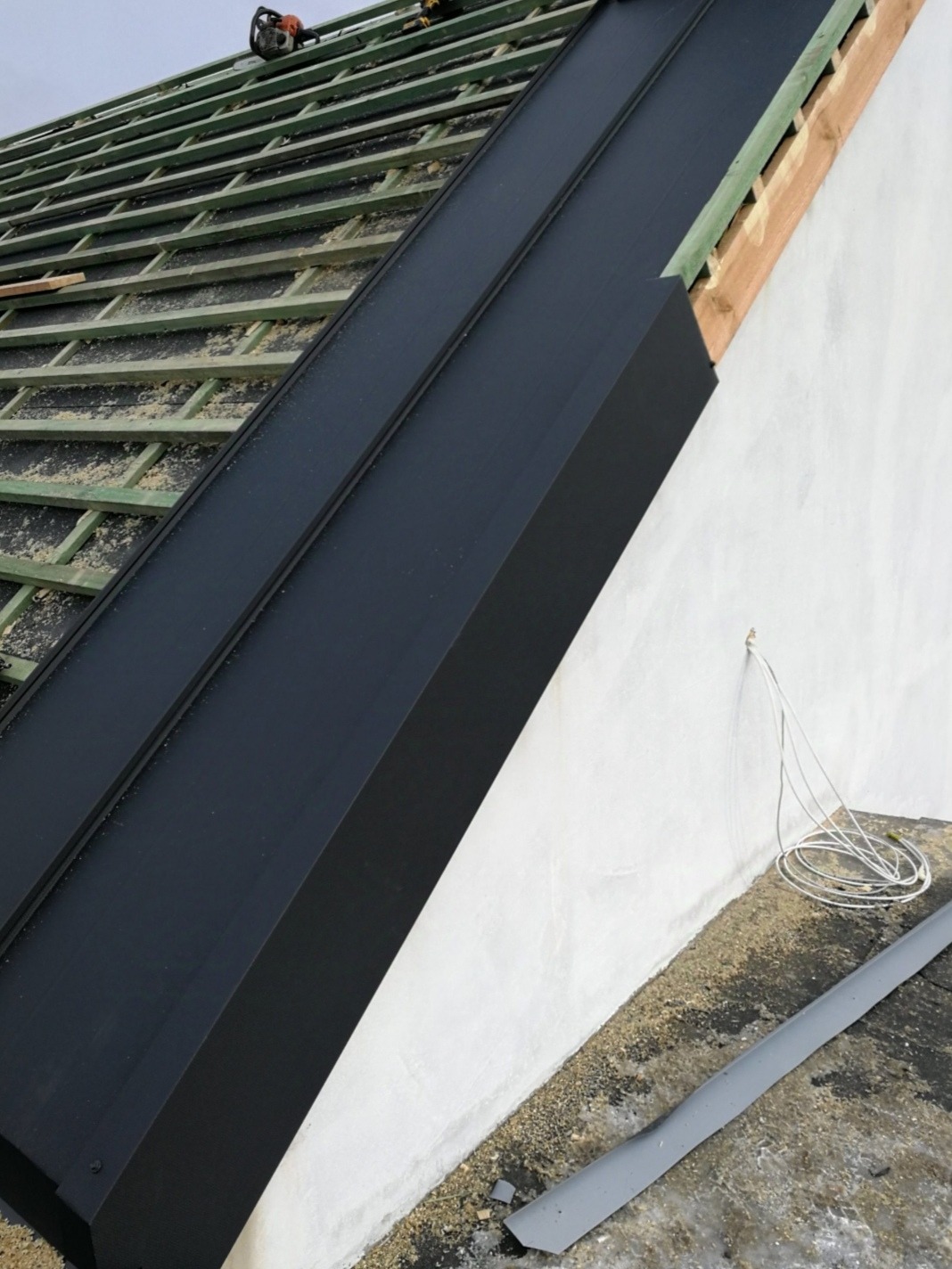 Częściowo pokryty dach z widoczną więźbą, czarnymi obróbkami blacharskimi i narzędziami na górze