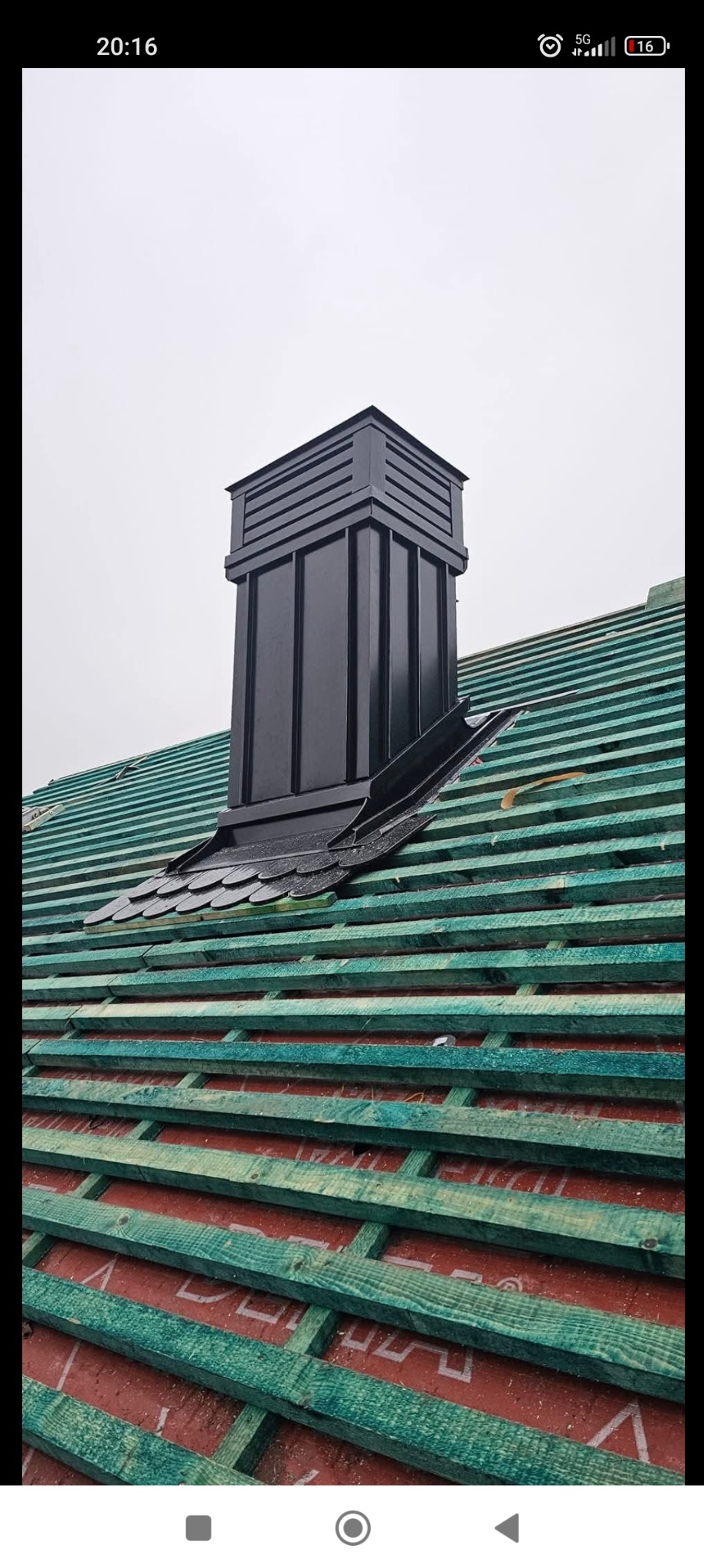 Nowy, czarny komin wentylacyjny na dachu z zielonej więźby i czerwonej membrany, widok z dołu.