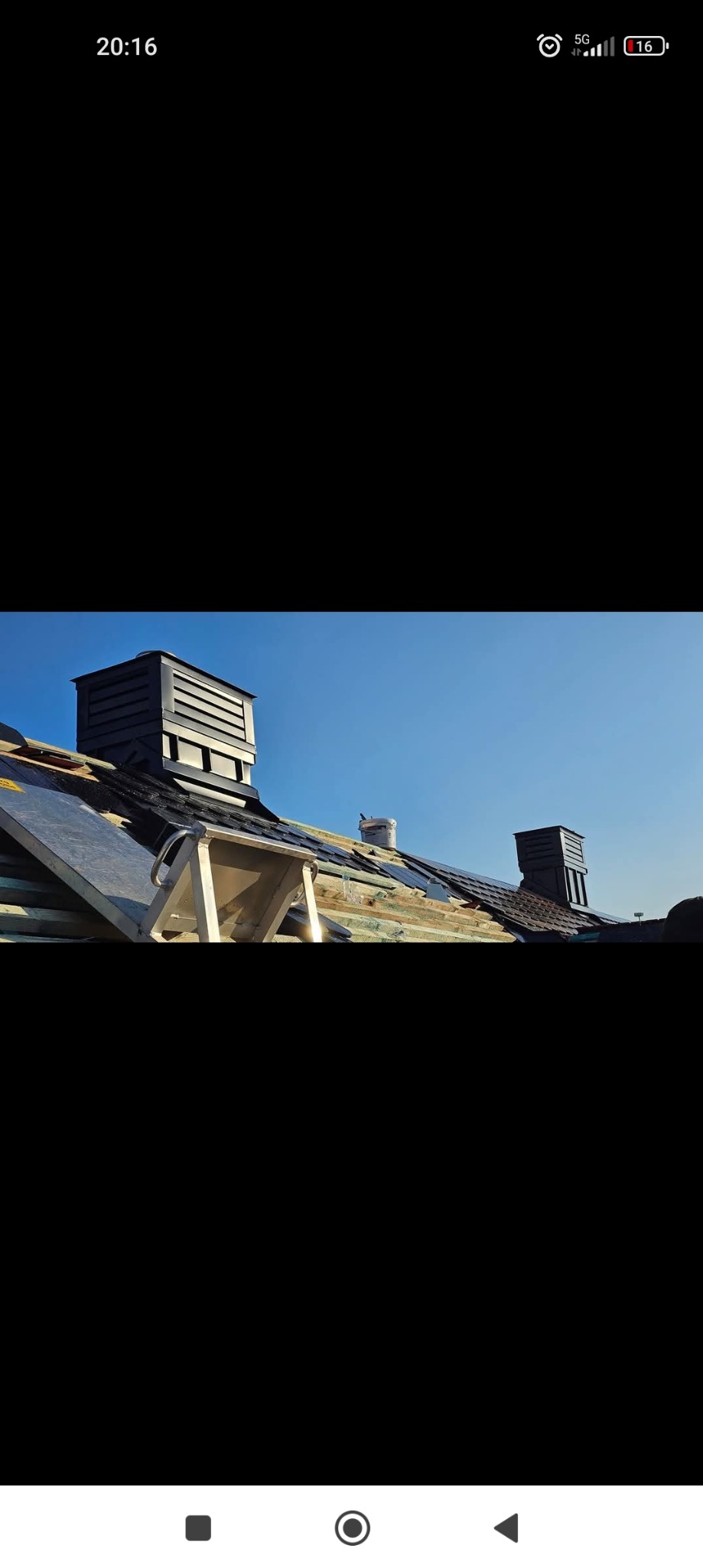 Fragment dachu w trakcie prac dekarskich z widocznymi elementami konstrukcji, nowymi dachówkami, dwoma kominami wentylacyjnymi z charakterystycznymi poziomymi szczelinami i podnośnikiem dekarskim...