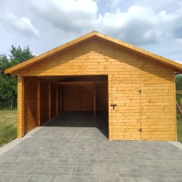 Kamil-drewniane wyroby - Drewniana altana z zamykaną częścią, świeżo po impregnacji, na wyłożonym kostką podłożu, w tle zieleń.