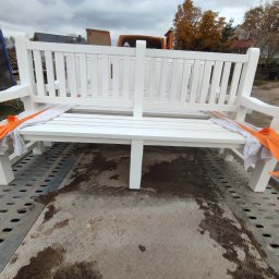 Kamil-drewniane wyroby - Nowa, biała, drewniana ławka ogrodowa zabezpieczona pomarańczowymi pasami transportowymi na przyczepie samochodowej.