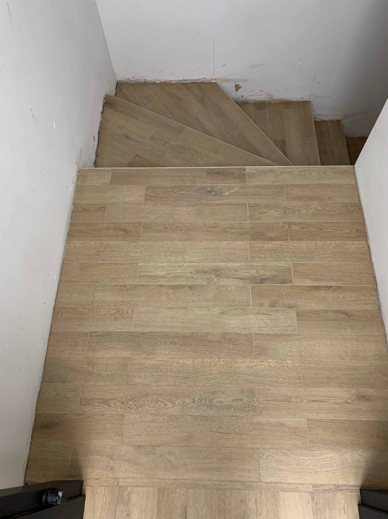 Wykończone schody i podłoga z płytek imitujących drewno, jasne odcienie, widok z góry, białe ściany. Układanie płytek w wąskim korytarzu.