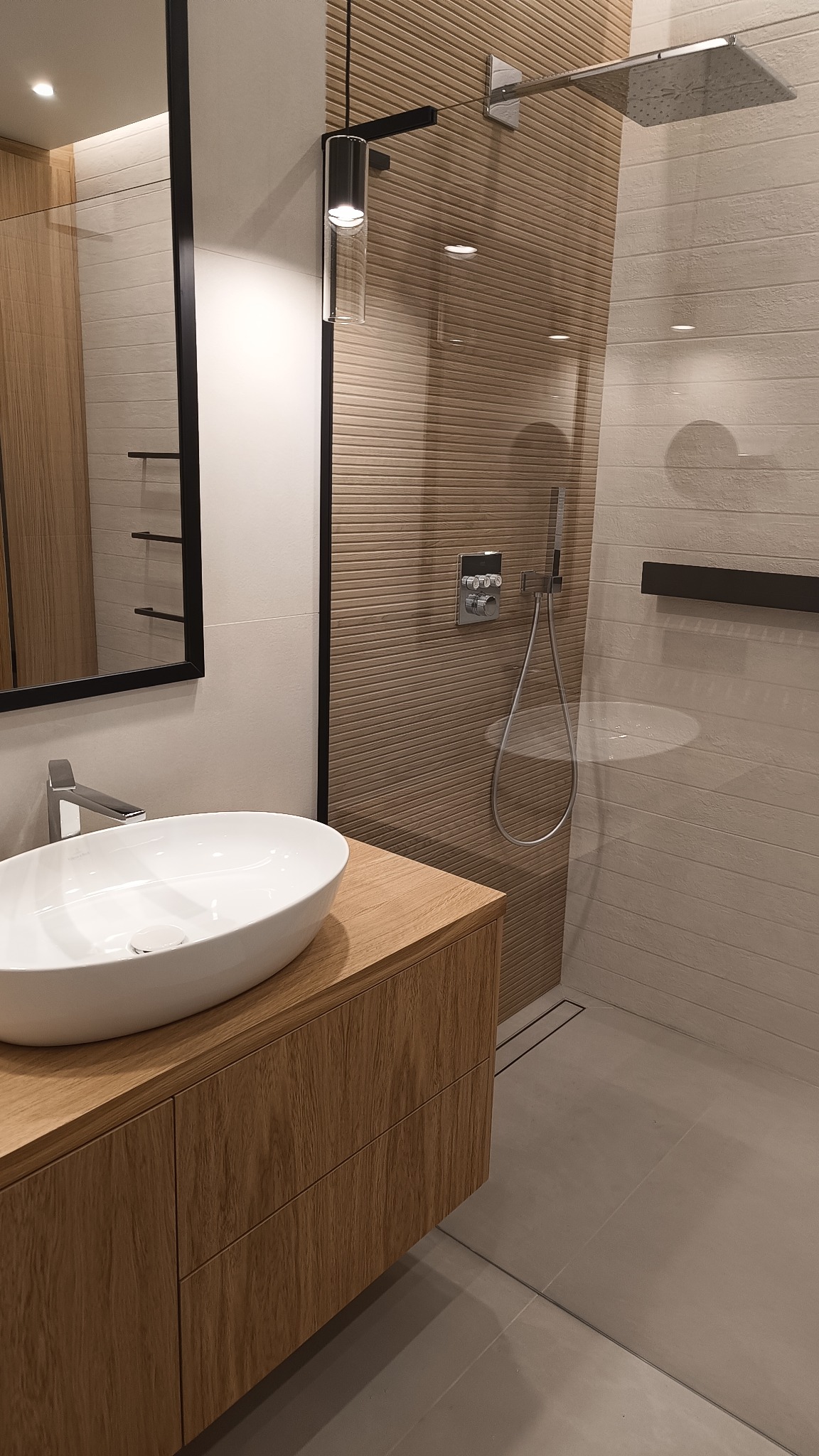 Nowoczesna łazienka z umywalką nablatową na drewnianej szafce, kabina prysznicowa typu walk-in z deszczownicą i panelami ściennymi o fakturze drewna w ciepłych odcieniach beżu.