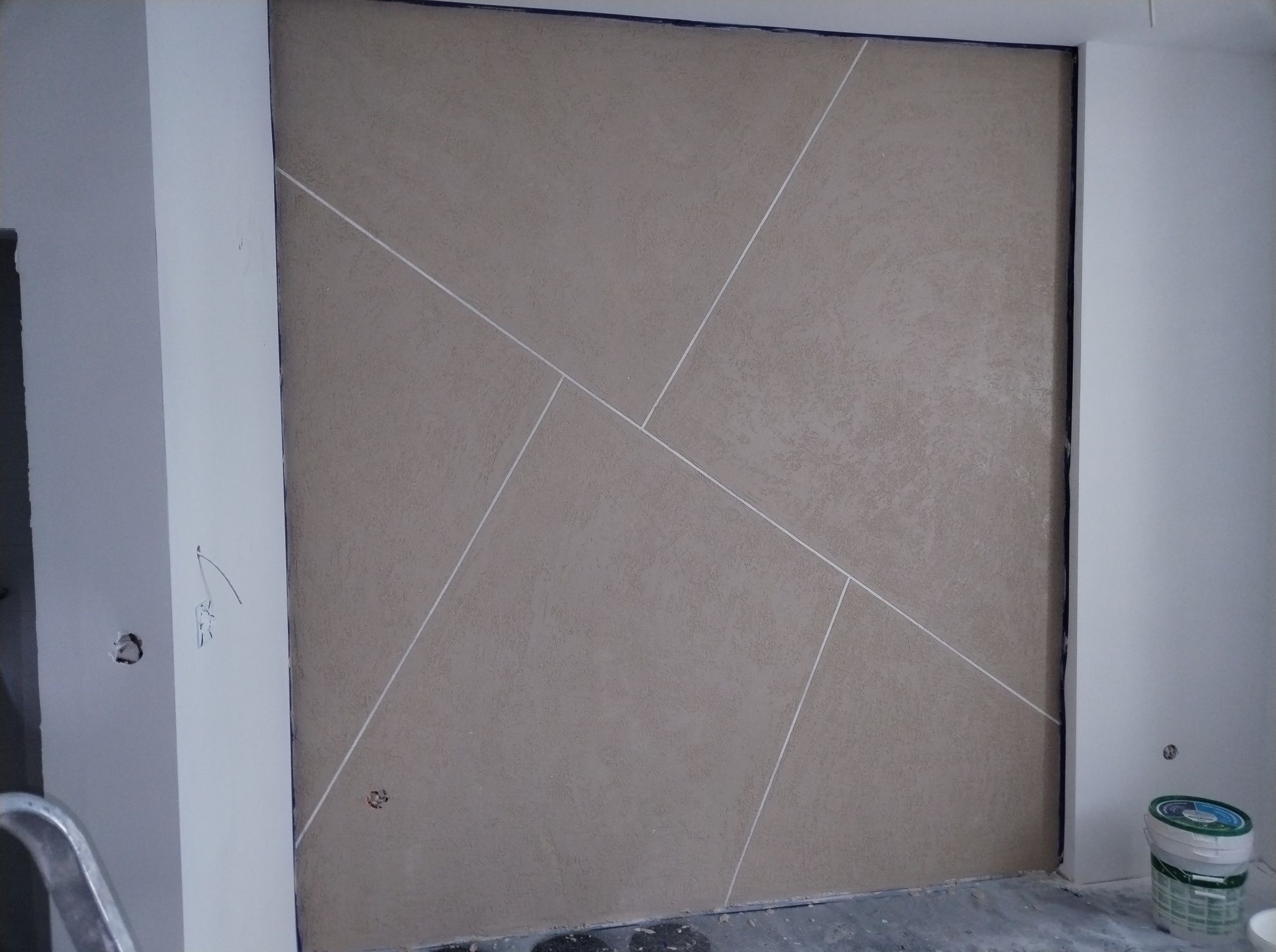 Dekoracyjna ściana beżowa z geometrycznym wzorem z białych linii. Widoczne puszki z farbą i fragment drabiny. Wykończenie wnętrz.