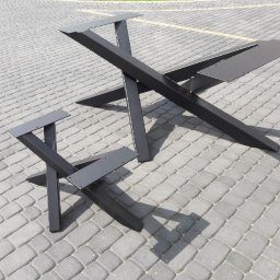PirSpawArt Rafał Pawełek - Dwie czarne, metalowe podstawy stołów o geometrycznym kształcie, ustawione na szarej kostce brukowej w słoneczny dzień. Większa podstawa ma kształt litery X z dodatkowymi elementami mocującymi,...