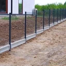 PirSpawArt Rafał Pawełek - Nowoczesne ogrodzenie panelowe z podmurówką betonową, widok z zewnątrz, częściowo zasypane ziemią, z klimatyzatorem na ścianie budynku w tle.