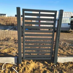 Nowoczesna, pozioma brama wjazdowa z metalowymi panelami, widoczna na tle ogrodzenia z siatki i białego samochodu dostawczego w słoneczny dzień.