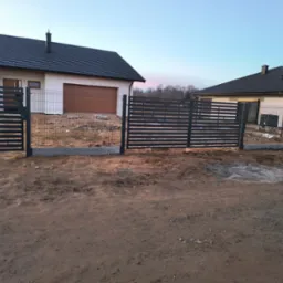 Nowoczesne, poziome przęsła ogrodzeniowe z metalu w kolorze grafitowym, oddzielające dwie posesje z nowymi domami jednorodzinnymi w trakcie wykańczania, widoczne świeże wylewki fundament&oacute;w...