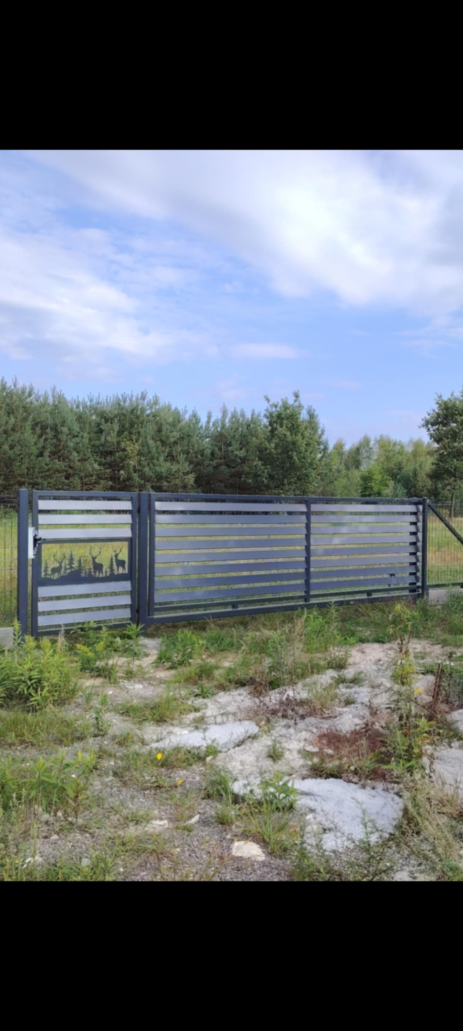 Nowoczesna brama wjazdowa z poziomymi panelami i dekoracyjnym motywem leśnym z sylwetkami jeleni, na tle zieleni i błękitnego nieba.