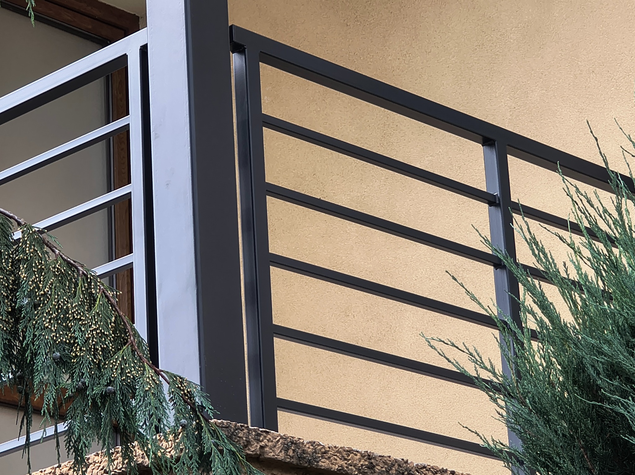 Nowoczesna, czarna balustrada balkonowa z poziomymi prętami, widok z dołu, z fragmentem zieleni po bokach. Eleganckie wykończenie balkonu.