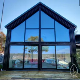 Nowoczesny dom z dużymi przeszkleniami w Skrzeszewie, z widokiem na jezioro, wykończony w ciemnej kolorystyce z drewnianym tarasem.