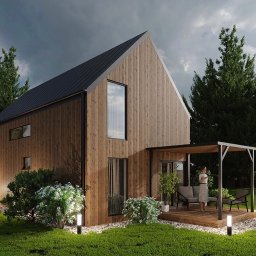 Skandic Hus - Nowoczesny dom z drewnianą elewacją, czarnym dachem i minimalistyczną pergolą, oświetlony lampami ogrodowymi, z kobietą stojącą na tarasie.