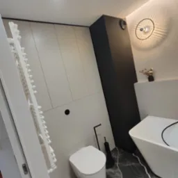 Nowoczesna łazienka w odcieniach szarości i czerni z marmurową posadzką, zabudową meblową pod sufit, wiszącą toaletą i wolnostojącą wanną.