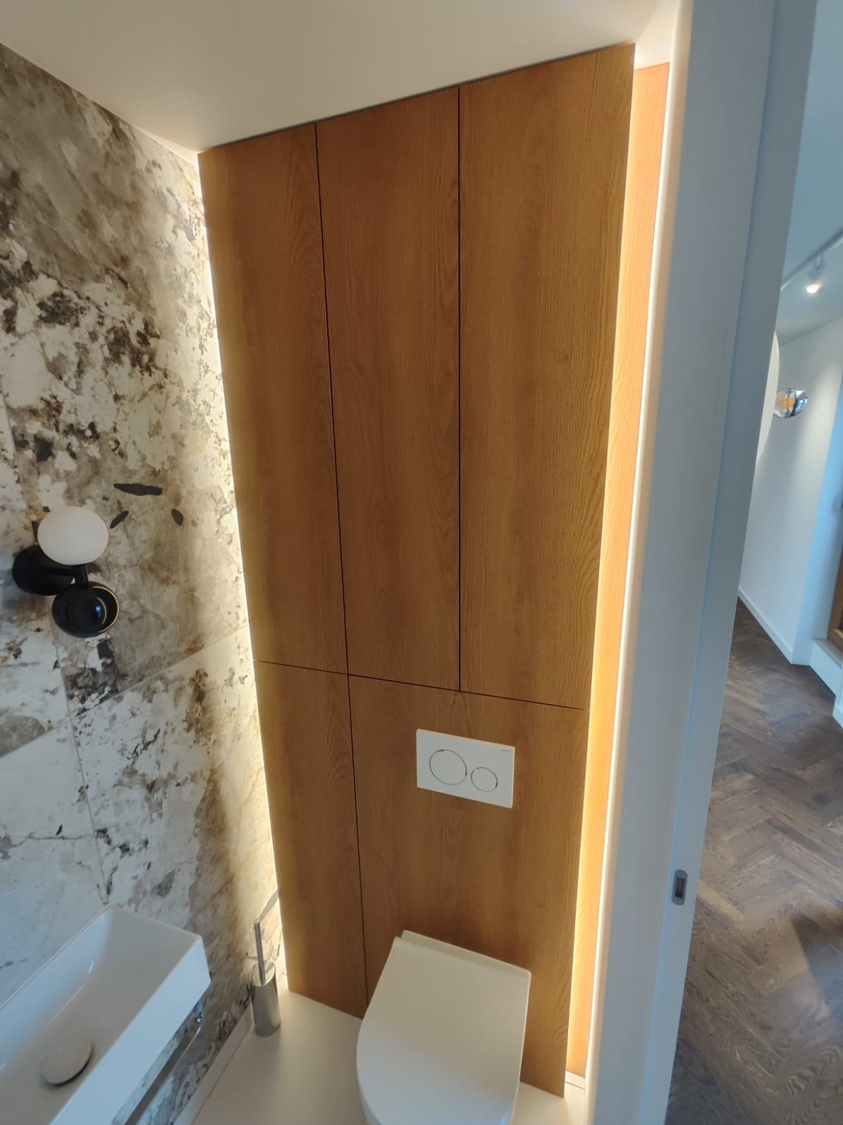 Nowoczesna łazienka z zabudową meblową z drewna z ukrytą spłuczką, umywalką nablatową i marmurową ścianą z designerską lampą.