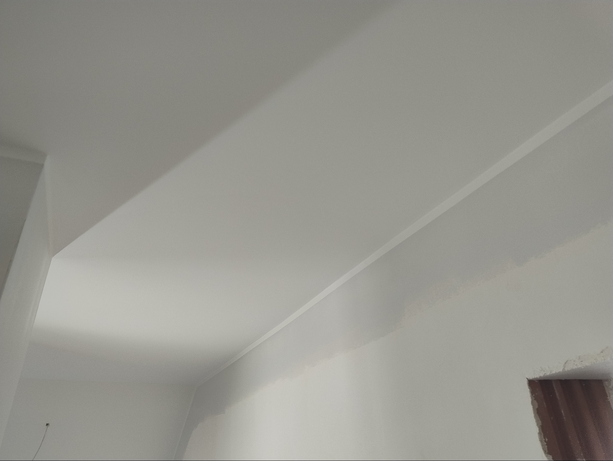 Fragment pomalowanego na biało sufitu i ściany z widocznym fragmentem otworu okiennego w stanie surowym.