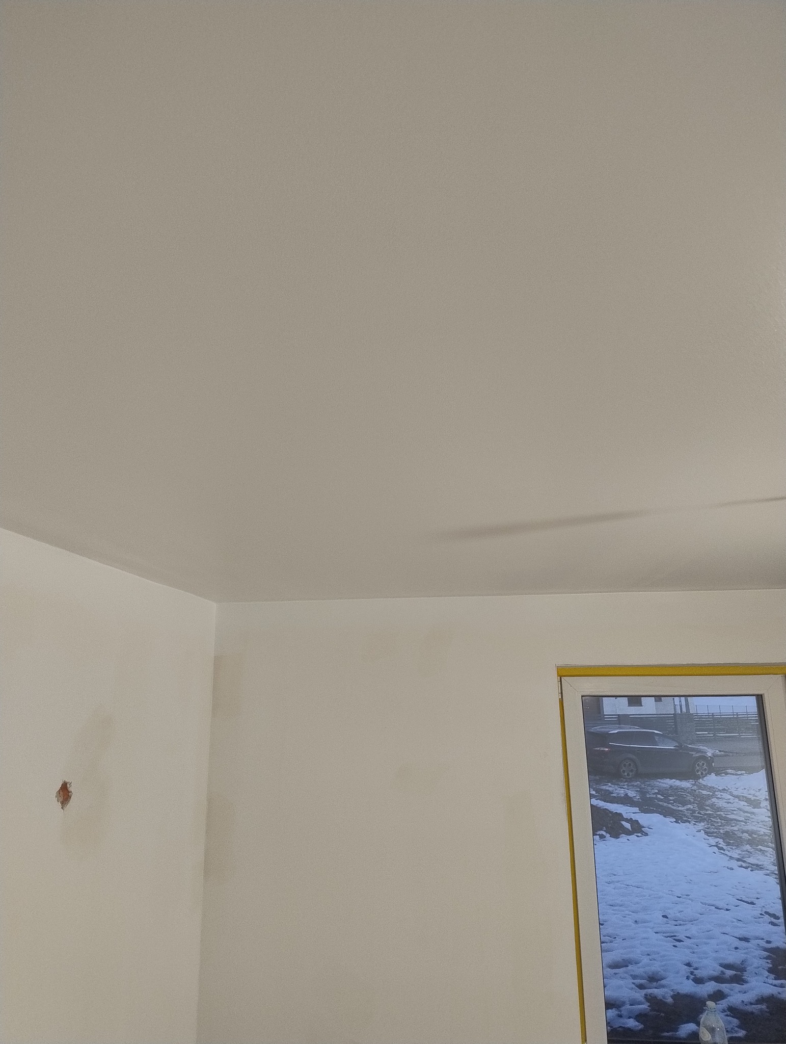 Świeżo pomalowane wnętrze z widocznymi śladami po szpachlowaniu i niewielkim ubytkiem na ścianie, okno z widokiem na zasnieżony krajobraz.