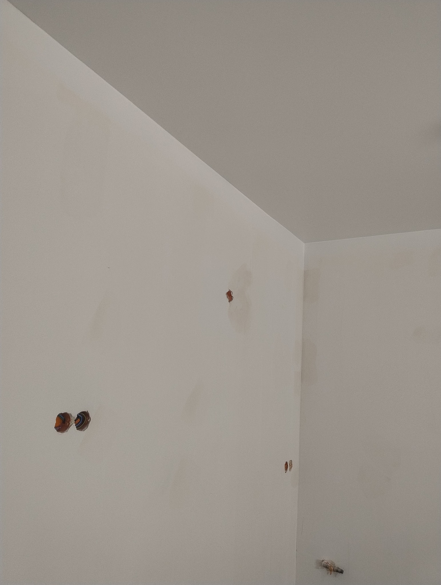 Ściana po szpachlowaniu, z widocznymi otworami po gniazdkach elektrycznych i niedoskonałościami przed malowaniem.