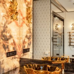 Visual Works Studio - Luksusowa łazienka: złota umywalka muszla na marmurowym blacie, podświetlana ściana z onyksu i ozdobne kinkiety w kształcie wachlarzy. Eleganckie wykończenie.