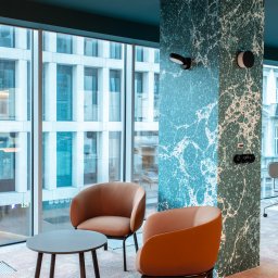 Visual Works Studio - Stylowe wnętrze biurowe: dwa fotele w odcieniach brązu przy okrągłym stoliku na tle marmurowej kolumny i dużego okna z widokiem na miasto. Nowoczesny design.