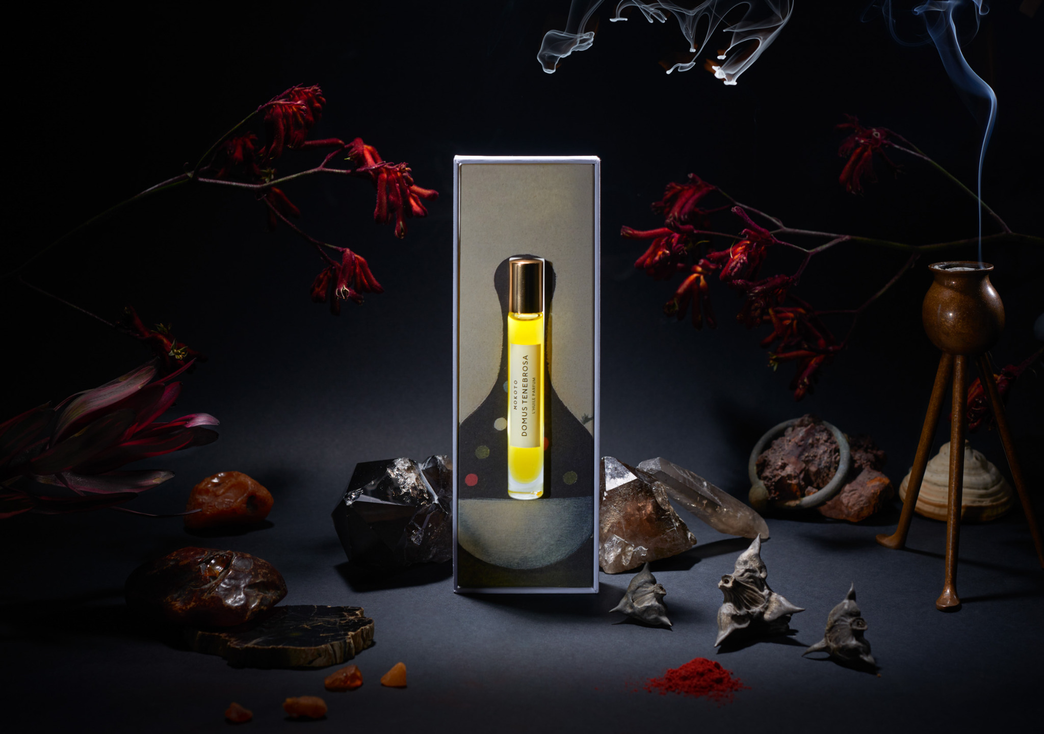 Artystyczne ujęcie flakonika perfum Mokoto Domus Tenebrosa w otoczeniu minerałów, kwiatów i dymu na ciemnym tle. Produkt w pudełku z abstrakcyjnym motywem.